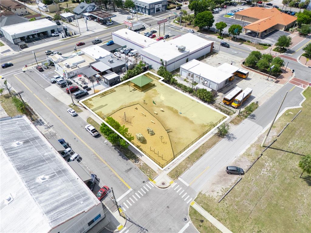 An aerial view shows a fenced-in playground lot situated between commercial buildings and streets — 165 5TH STREET SW, WINTER HAVEN, FL