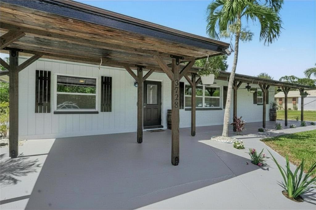 A white house exterior features a long covered porch with wooden posts and a palm tree — 3728 GASPARILLA STREET, ST JAMES CITY, FL