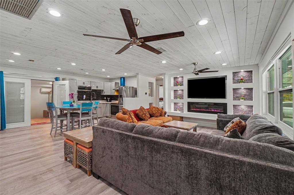 An open-concept living room and kitchen featuring a gray sectional, fireplace, and white plank ceiling — 3728 GASPARILLA STREET, ST JAMES CITY, FL