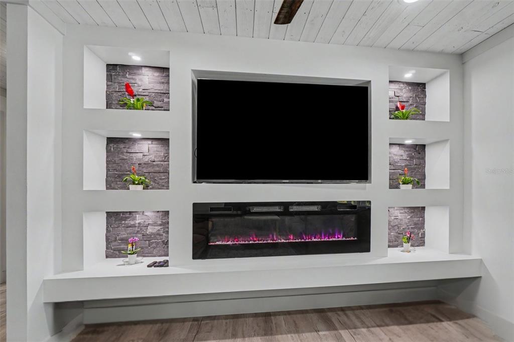A living room wall features a built-in television, electric fireplace, and recessed stone-backed shelving — 3728 GASPARILLA STREET, ST JAMES CITY, FL
