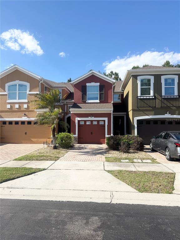 Three attached townhomes with garages and driveways stand under a clear blue sky — 9319 STRONGBARK LANE, ORLANDO, FL