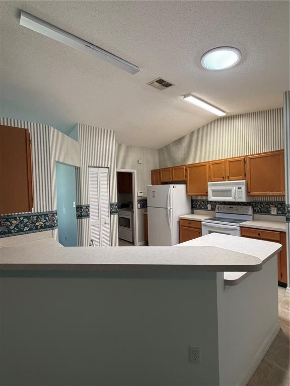 A kitchen with wood cabinets, white appliances, striped wallpaper, and a breakfast bar — 6087 KITTIWAKE DRIVE, LAKELAND, FL