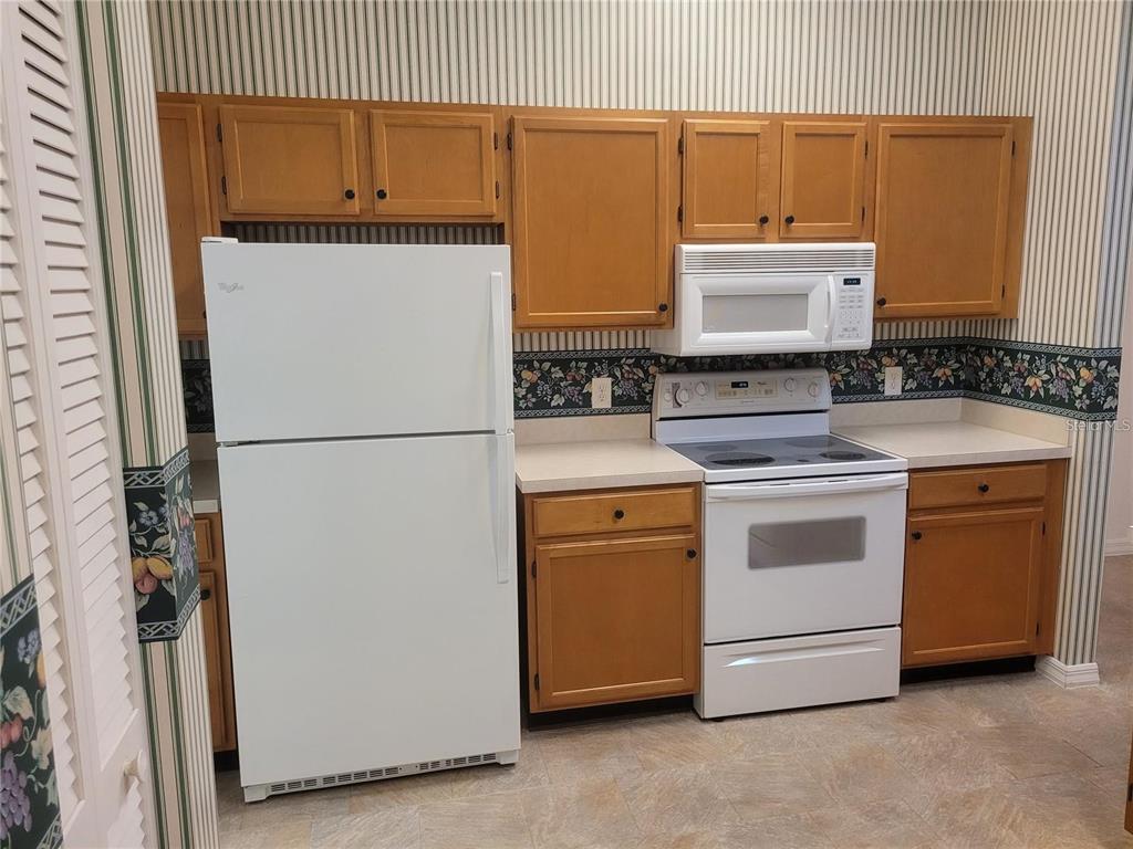 A kitchen features light wood cabinets, white appliances, and wallpaper with a floral border — 6087 KITTIWAKE DRIVE, LAKELAND, FL