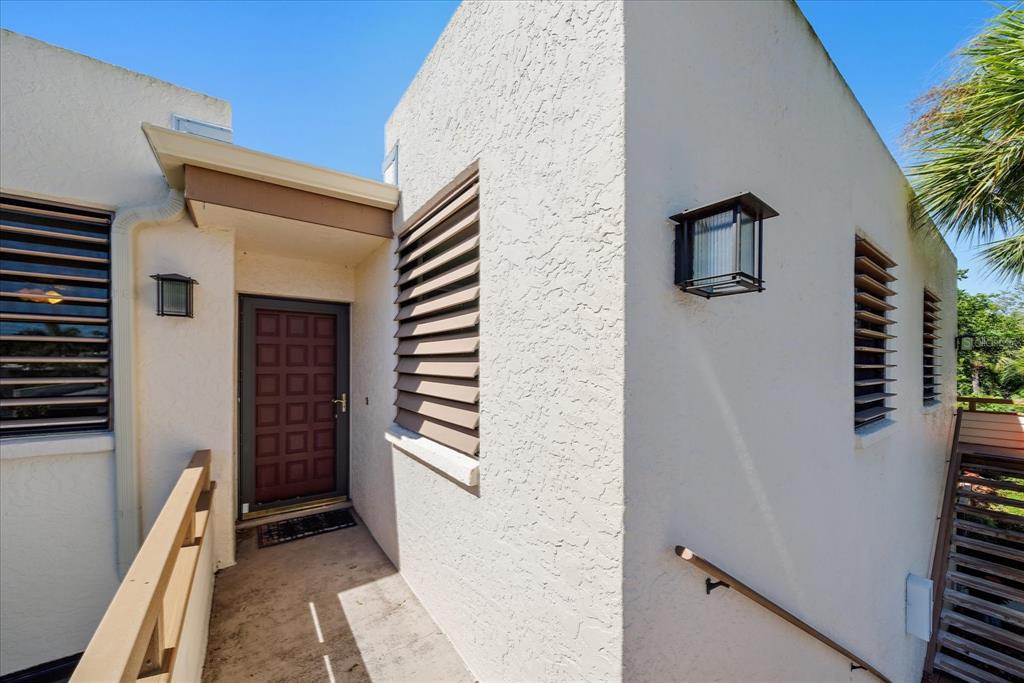 An exterior view shows a white stucco building entrance with a brown door and shutters — 182 PINENEEDLE DRIVE, BRADENTON, FL