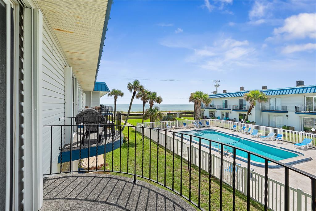 A balcony overlooks a swimming pool, green lawn, and the ocean in the distance — 2750 OCEAN SHORE BOULEVARD UNIT 430, ORMOND BEACH, FL