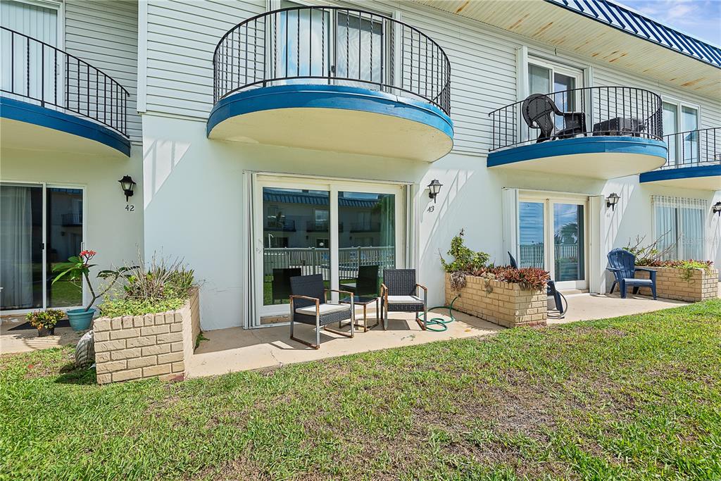 The exterior of a multi-story building features ground-level patios with brick planters and upper-level balconies — 2750 OCEAN SHORE BOULEVARD UNIT 430, ORMOND BEACH, FL