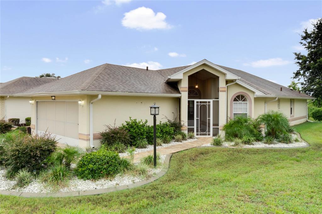 A single-story house with a beige exterior, a two-car garage, and a screened front entryway — 21721 KING RICHARDS WAY, LEESBURG, FL