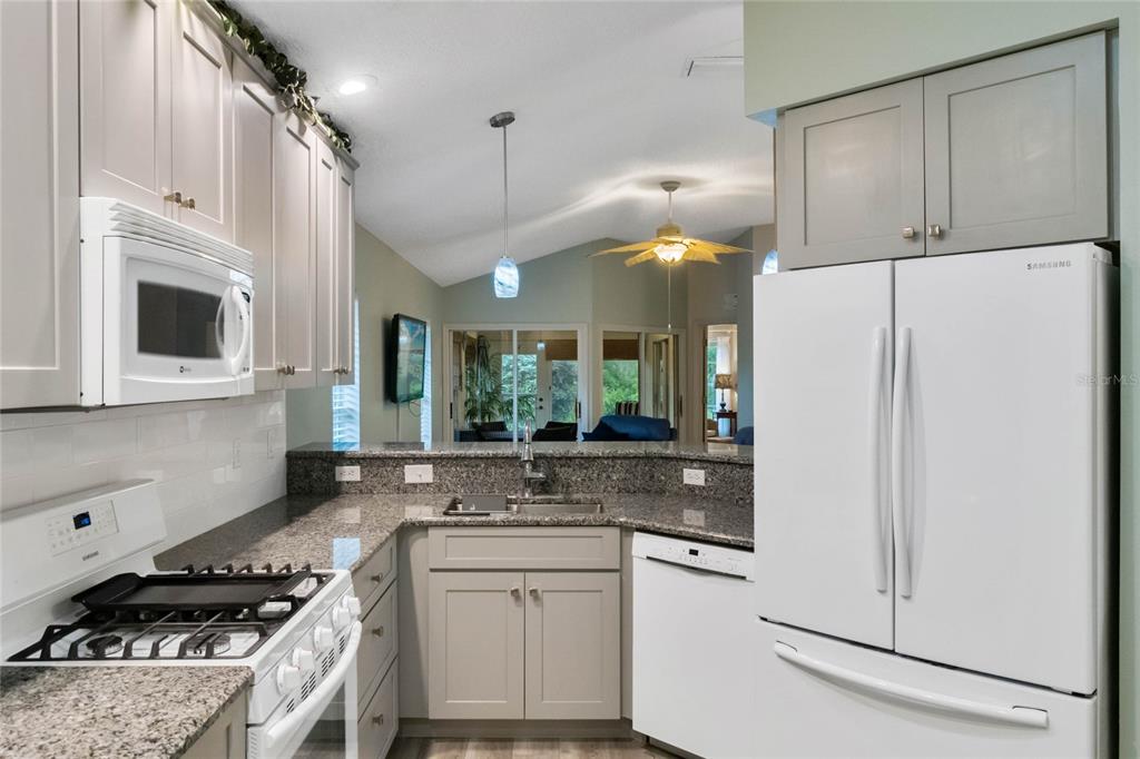 A kitchen features light gray cabinets, granite countertops, white appliances, and a pass-through sink area — 21721 KING RICHARDS WAY, LEESBURG, FL