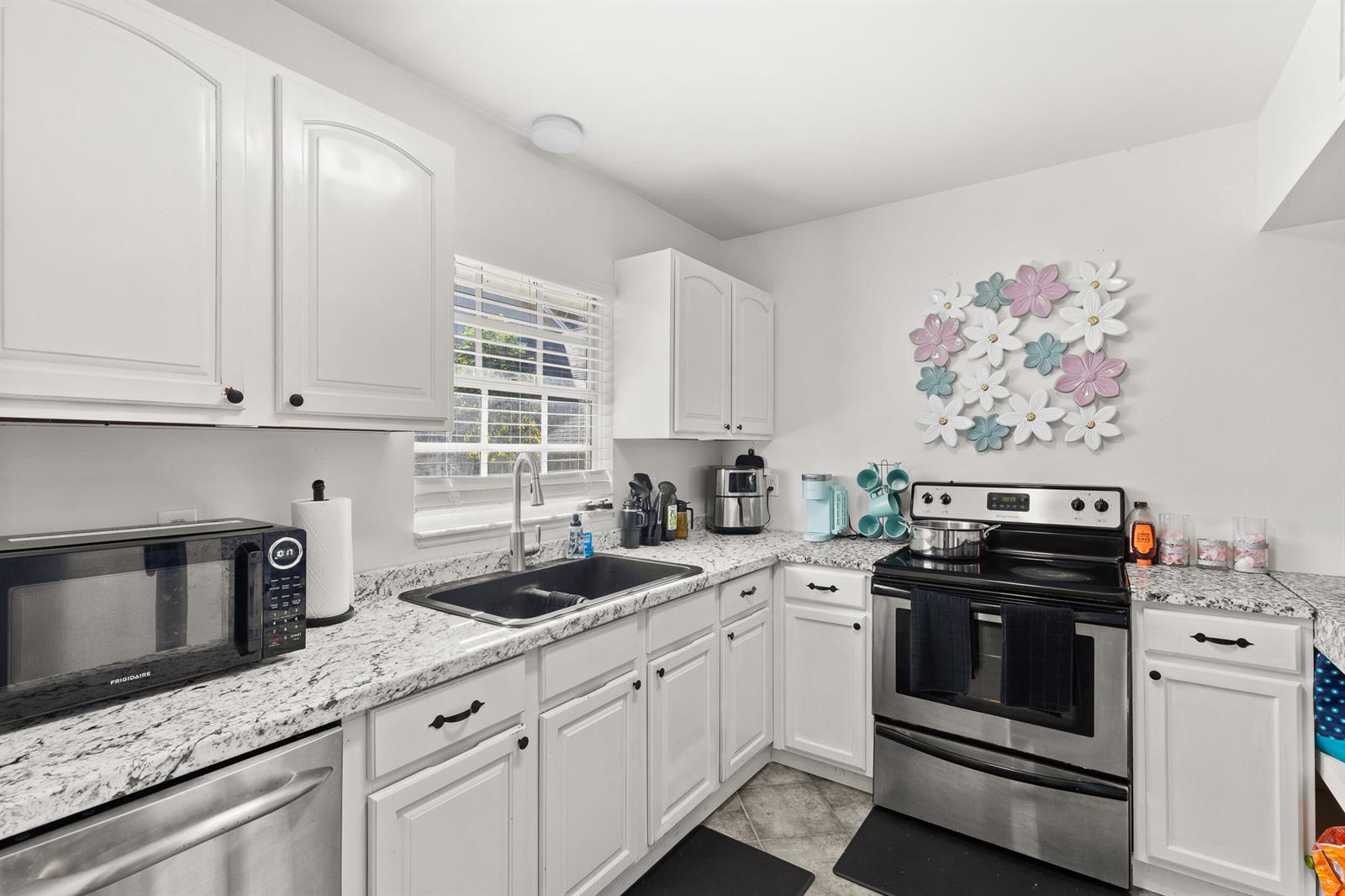 A kitchen with white cabinets, granite countertops, stainless steel appliances, and a floral wall decoration — 1329 Villa Lane # 45, FL 32712, FL