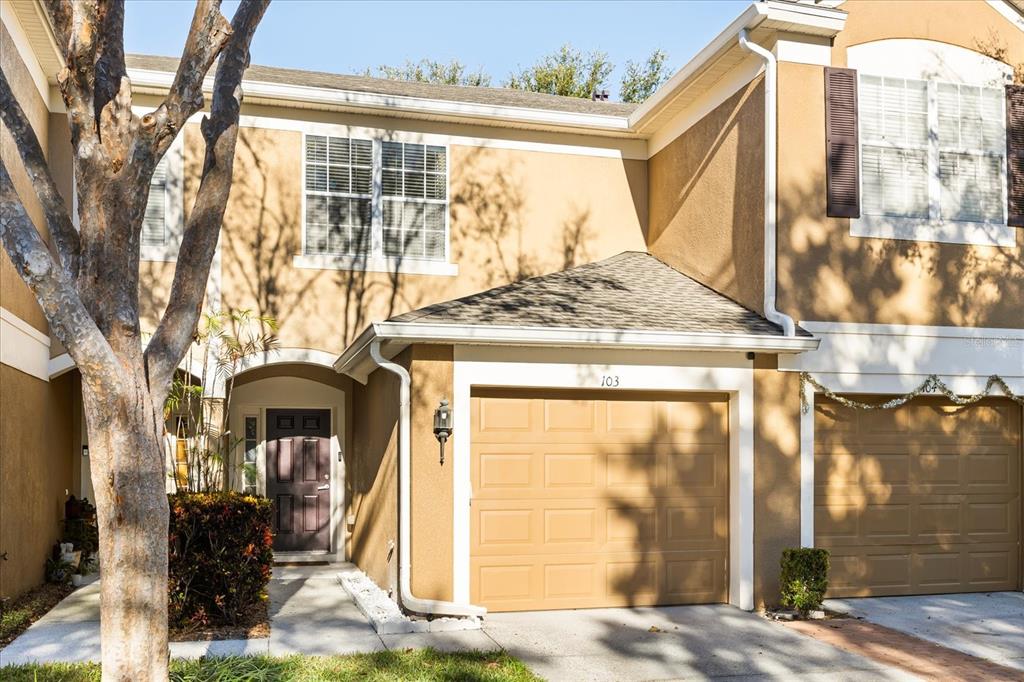 A two-story tan townhouse with a single-car garage, a dark front door, and a tree — 2804 POLVADERO LANE UNIT 103, ORLANDO, FL