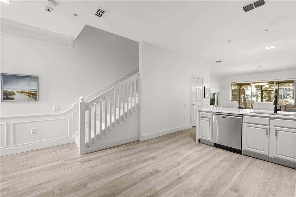 A bright kitchen and living area features white cabinetry, stainless appliances, and a wooden staircase — 2804 POLVADERO LANE UNIT 103, ORLANDO, FL
