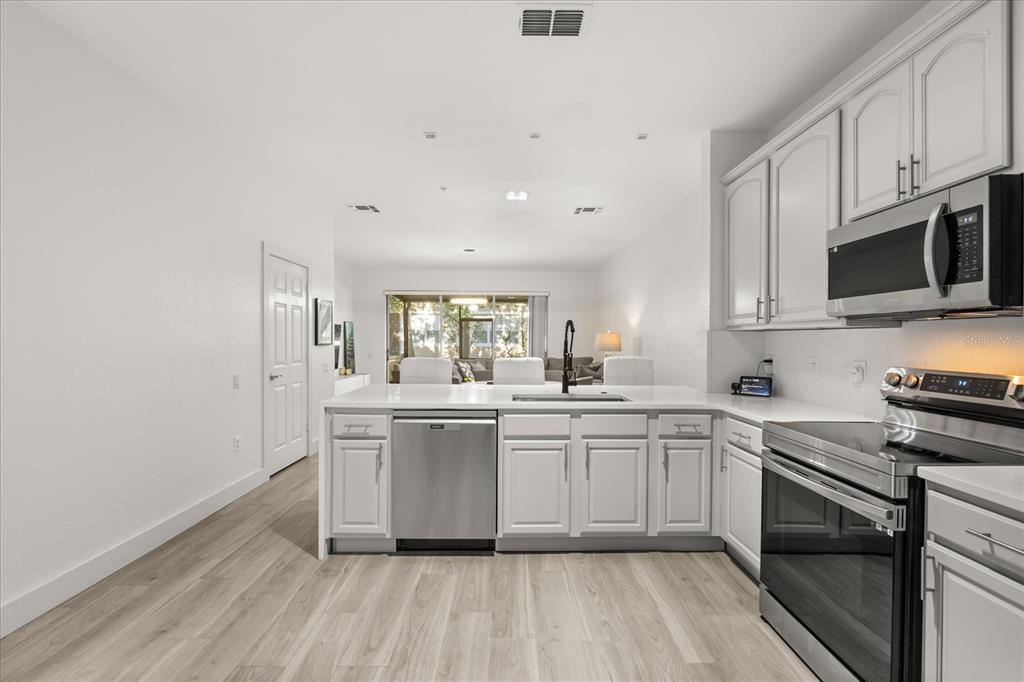 A kitchen with white cabinets, stainless steel appliances, and light wood-look flooring — 2804 POLVADERO LANE UNIT 103, ORLANDO, FL