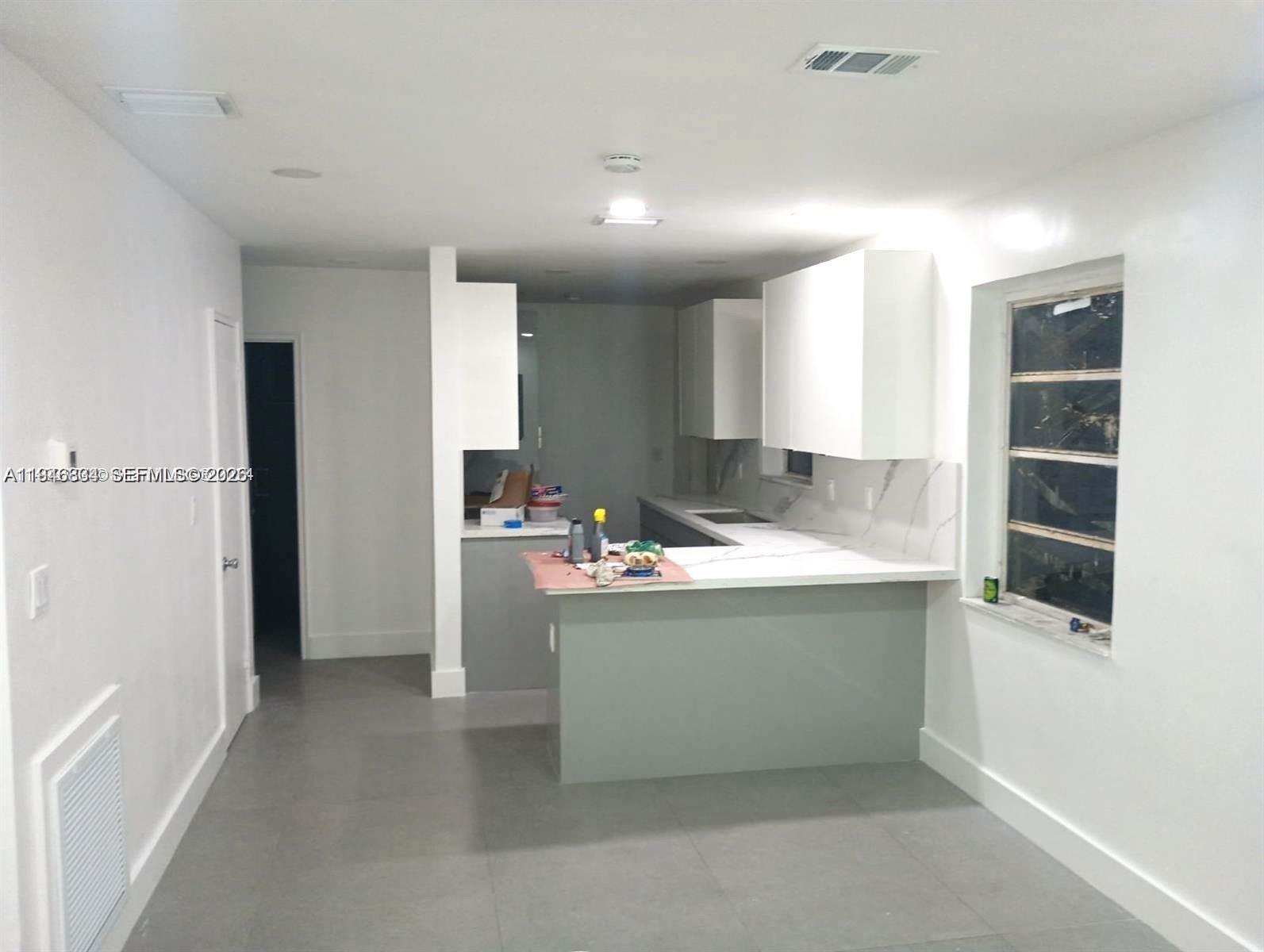 A kitchen features white upper cabinets, gray lower cabinets, and a white countertop peninsula — 110 NW 120 Ter, North Miami FL 33168, NORTH MIAMI, FL