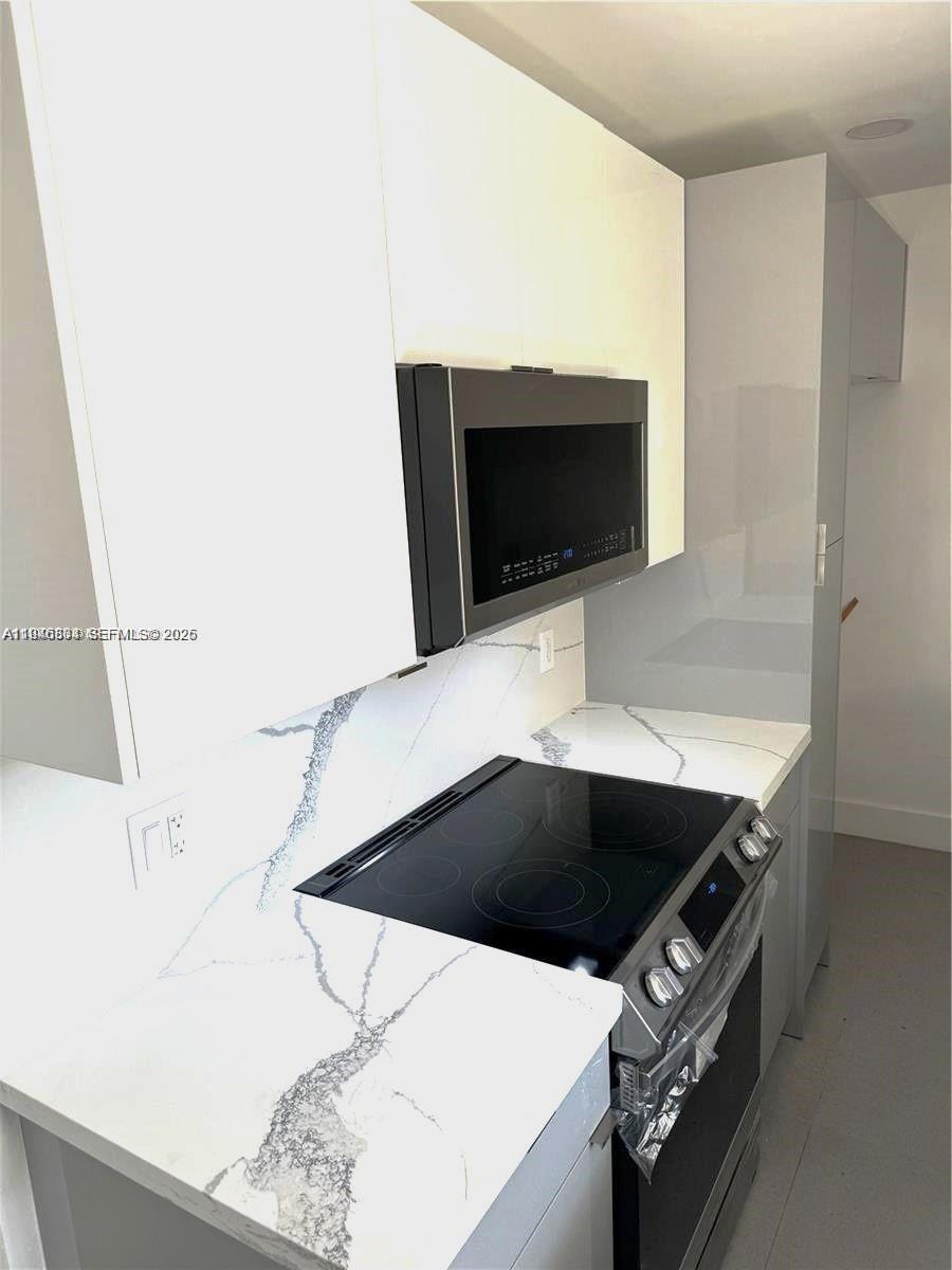 A modern kitchen features white cabinets, a stainless steel microwave, and a marble-patterned countertop — 110 NW 120 Ter, North Miami FL 33168, NORTH MIAMI, FL
