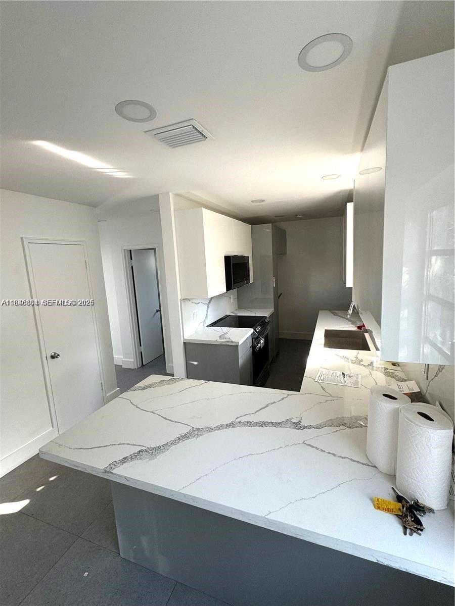 A modern kitchen features white cabinets, gray lower cabinets, and a white marble-patterned countertop — 110 NW 120 Ter, North Miami FL 33168, NORTH MIAMI, FL