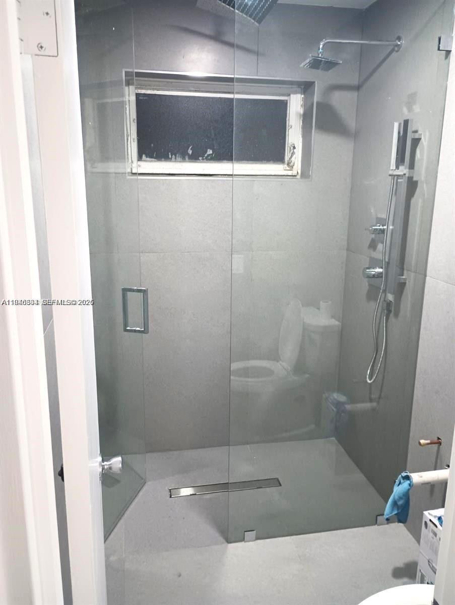 A walk-in shower with gray tile walls and a glass door contains a toilet — 110 NW 120 Ter, North Miami FL 33168, NORTH MIAMI, FL