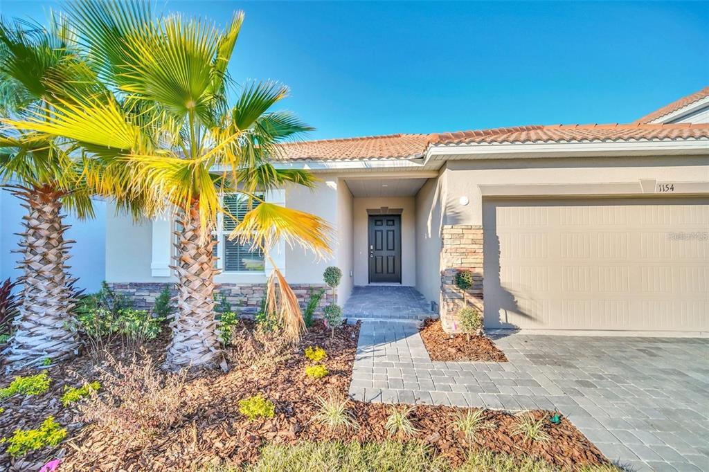 A single-story house exterior features a paved walkway, a palm tree, and a stone-accented entryway — 1154 OAK BLUFF DRIVE, DAVENPORT, FL
