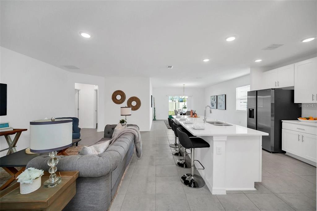An open-concept living room and kitchen featuring a gray sofa, white island, and tile flooring — 1154 OAK BLUFF DRIVE, DAVENPORT, FL