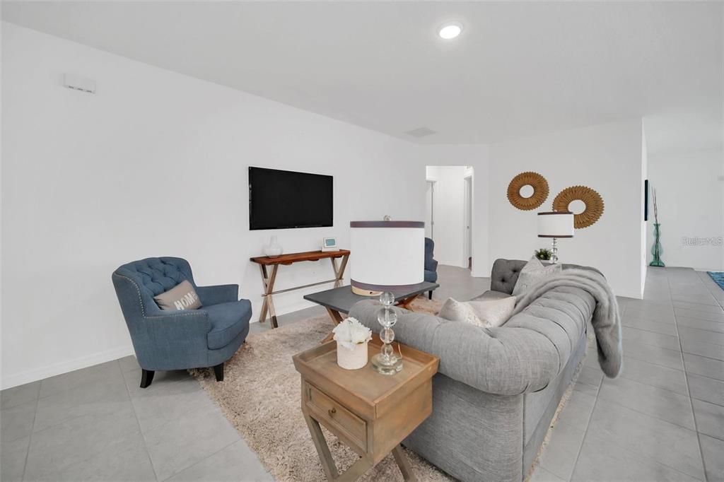 A living room features a grey tufted sofa, a blue armchair, and a wall-mounted television — 1154 OAK BLUFF DRIVE, DAVENPORT, FL