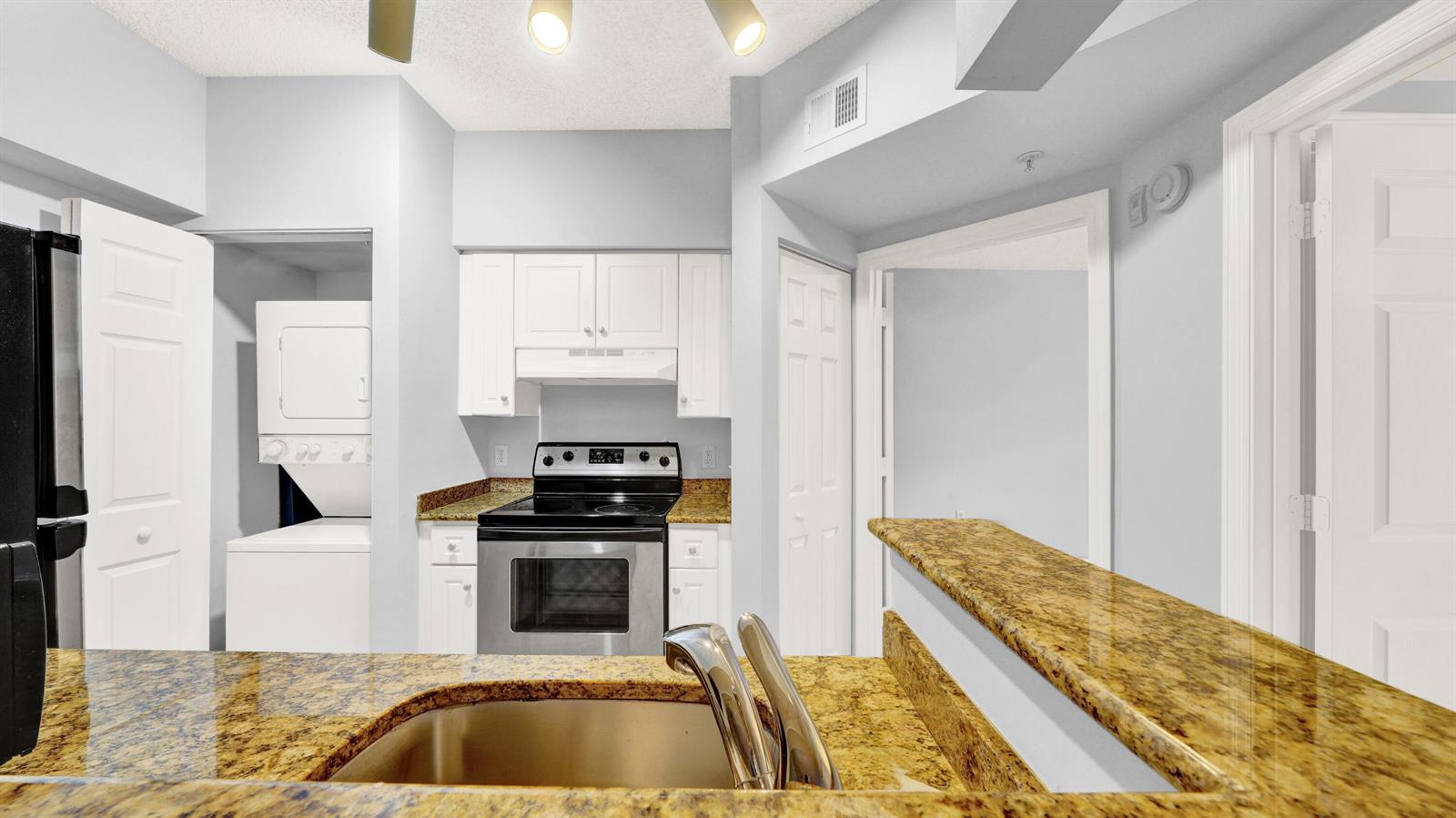 A kitchen features white cabinets, granite countertops, stainless steel appliances, and an in-unit laundry closet — 3106 Tuscany Way, Boynton Beach FL 33435, BOYNTON BEACH, FL