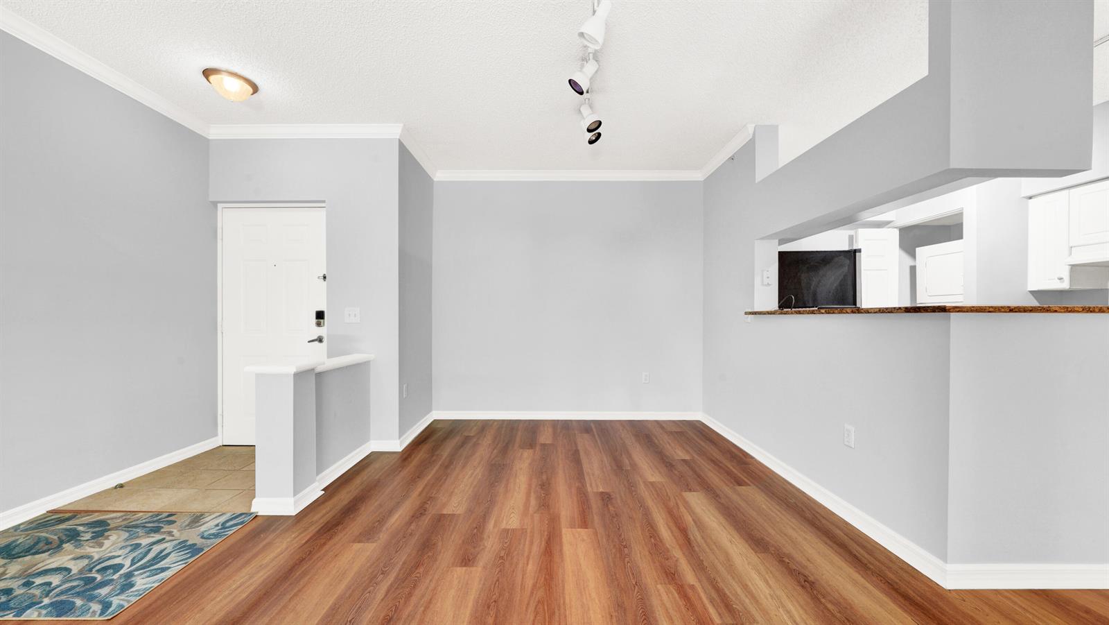 An empty room with light gray walls, wood-look flooring, and a kitchen pass-through window — 3106 Tuscany Way, Boynton Beach FL 33435, BOYNTON BEACH, FL