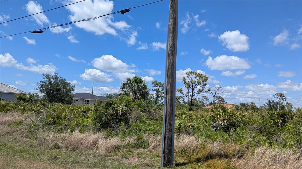 A utility pole stands in the foreground of a grassy, overgrown lot under a blue sky — 13474 ABUTILON LANE, PORT CHARLOTTE, FL