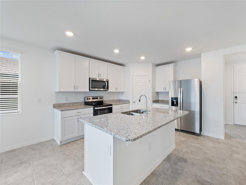A modern kitchen features white cabinets, granite countertops, a center island, and stainless steel appliances — 2606 IRISH ELK AVENUE, DAVENPORT, FL