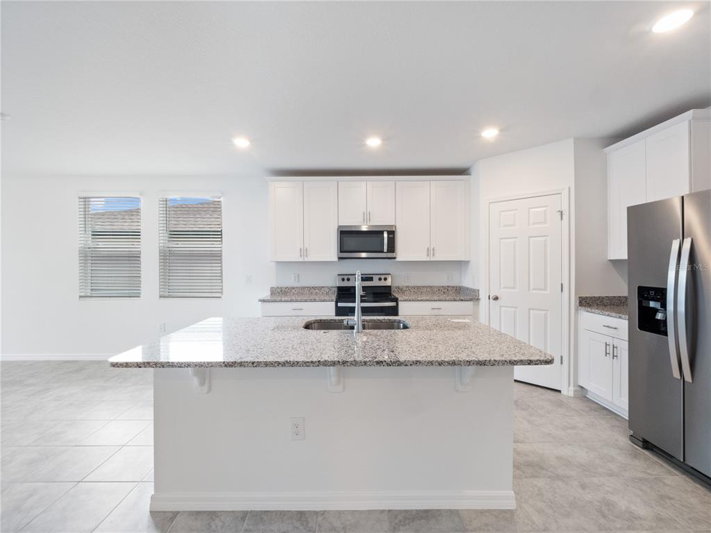 A kitchen features white cabinets, granite countertops, a central island, and stainless steel appliances — 2606 IRISH ELK AVENUE, DAVENPORT, FL