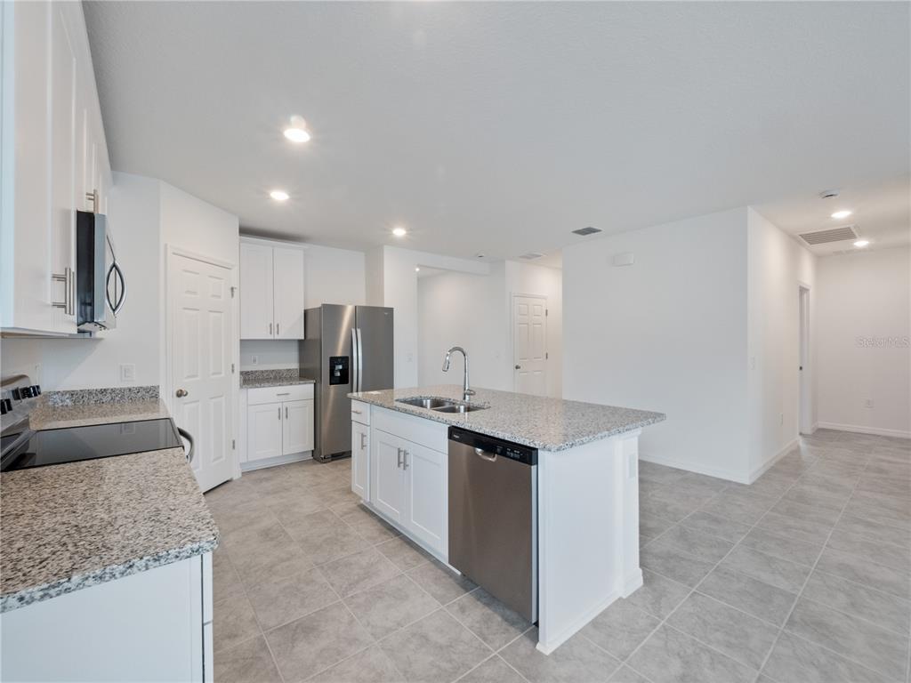 A kitchen features white cabinets, granite countertops, stainless steel appliances, and gray tile flooring — 2606 IRISH ELK AVENUE, DAVENPORT, FL