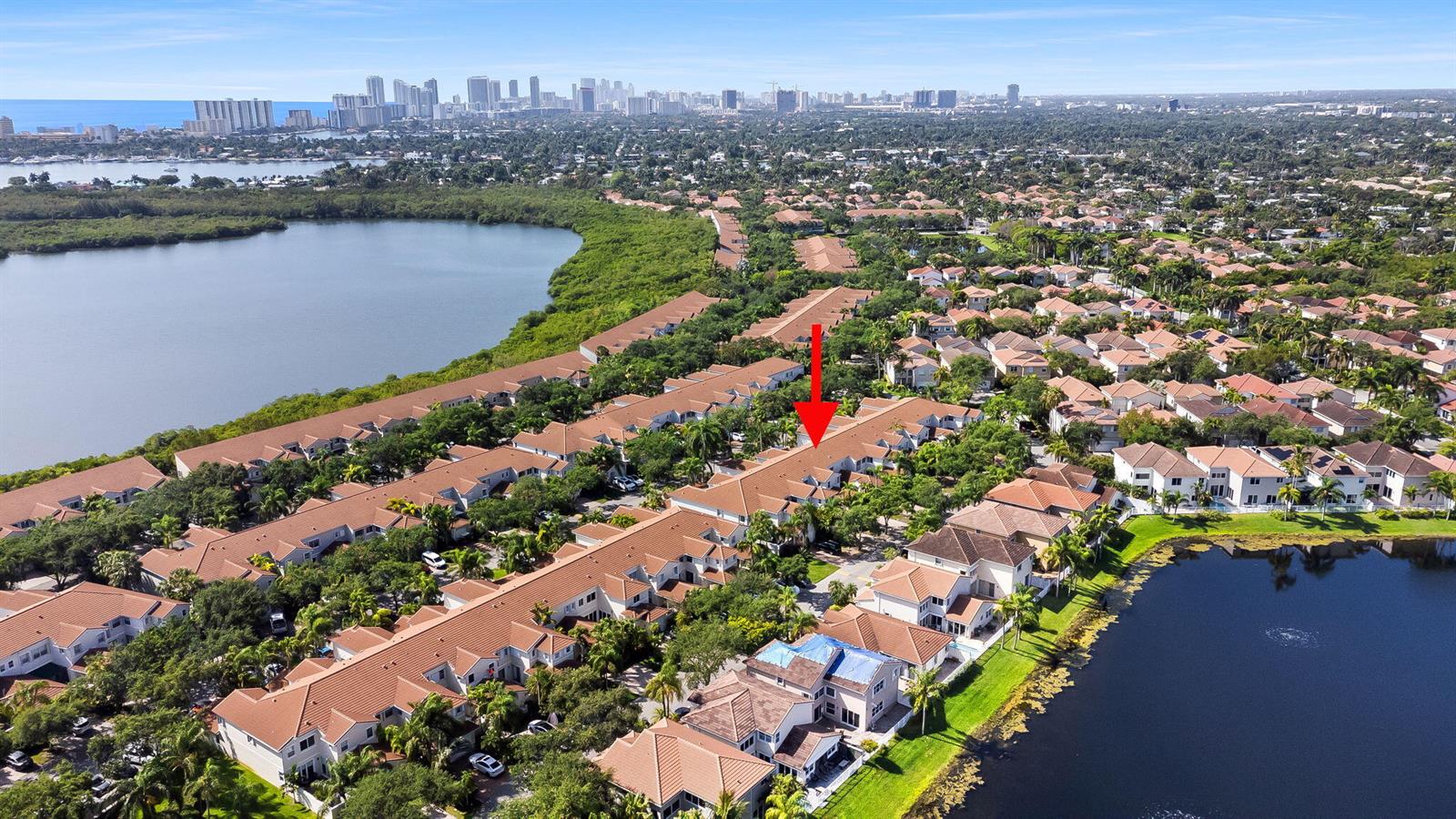 An aerial view shows a residential townhouse complex with tile roofs near a large lake — 1551 Seagrape Way, Hollywood FL 33019, HOLLYWOOD, FL
