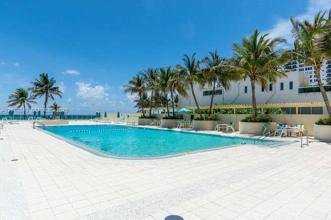 An outdoor swimming pool surrounded by a tiled deck and palm trees under a blue sky — 2501 S OCEAN DR # 637, Hollywood FL 33019, HOLLYWOOD, FL