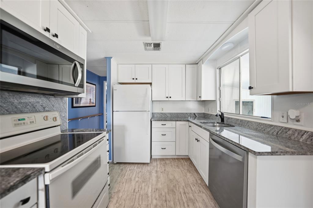 A kitchen features white cabinets, granite countertops, stainless steel appliances, and light wood-look flooring — 195 S FIJI CIRCLE, ENGLEWOOD, FL