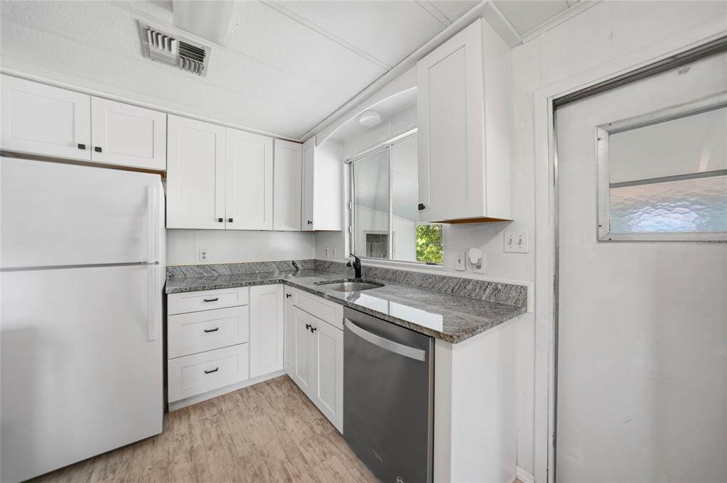 A kitchen features white cabinets, granite countertops, stainless steel appliances, and light wood-look flooring — 195 S FIJI CIRCLE, ENGLEWOOD, FL