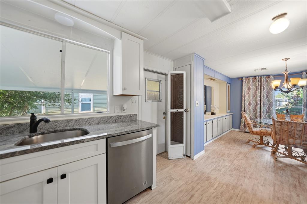 A kitchen with granite countertops, stainless steel dishwasher, and an adjacent dining area with chandelier — 195 S FIJI CIRCLE, ENGLEWOOD, FL