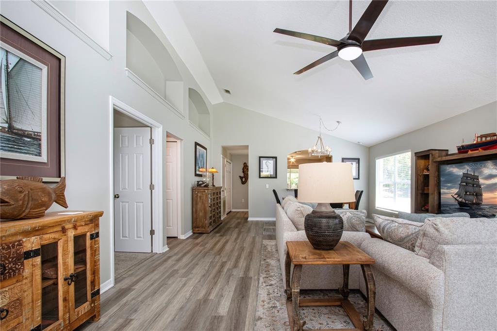 A living room features vaulted ceilings, wood-look flooring, a ceiling fan, and nautical decor — 12341 WOOD SAGE TERRACE, BRADENTON, FL