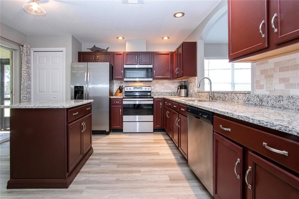 A kitchen features dark wood cabinets, granite countertops, stainless steel appliances, and light wood flooring — 12341 WOOD SAGE TERRACE, BRADENTON, FL
