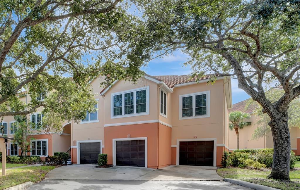 A multi-story residential building with three garage doors and large oak trees in the foreground — 4110 CENTRAL SARASOTA PARKWAY UNIT 125, SARASOTA, FL