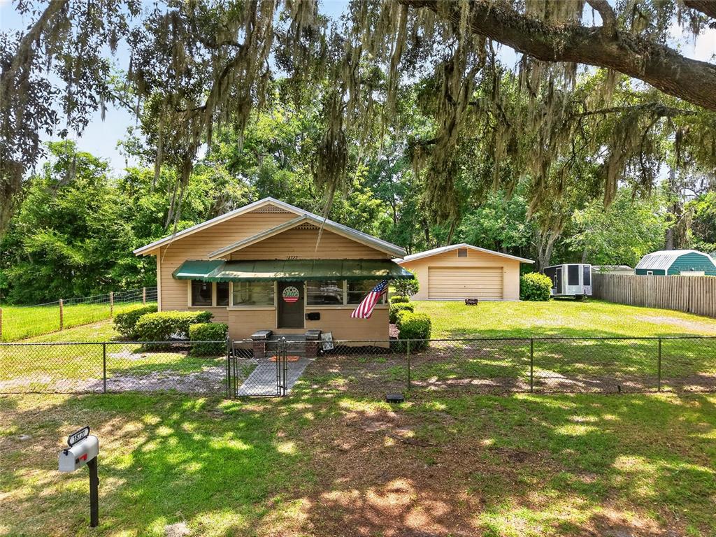 A single-story house with a detached garage sits on a grassy lot behind a fence — 18727 NW 251ST STREET, HIGH SPRINGS, FL