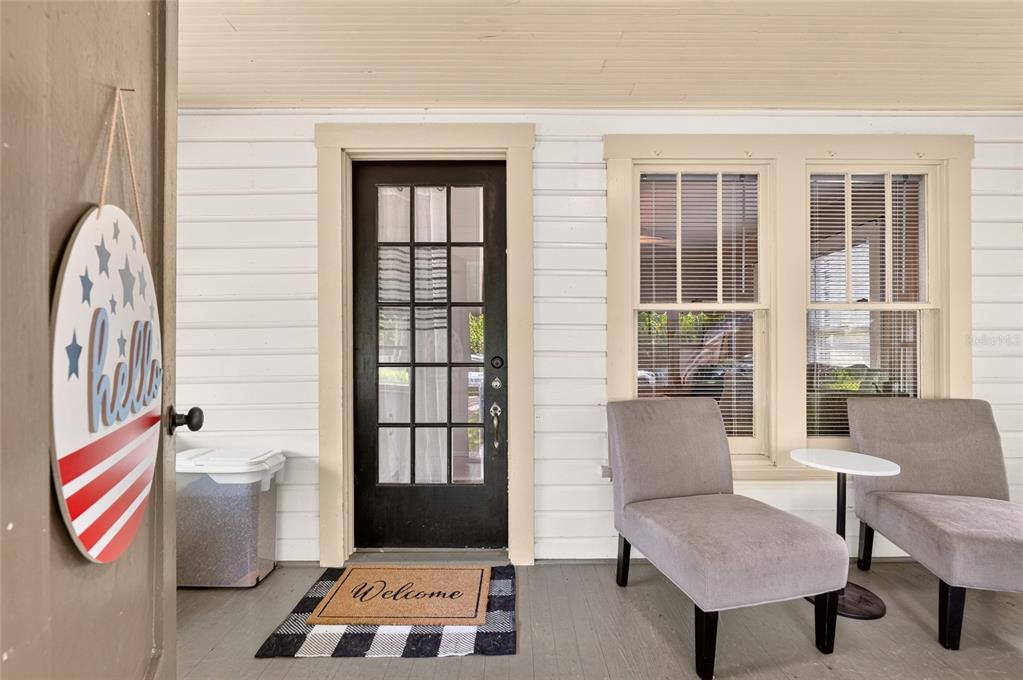 A covered front porch features a black glass-paneled door, two gray chairs, and patriotic decor — 18727 NW 251ST STREET, HIGH SPRINGS, FL