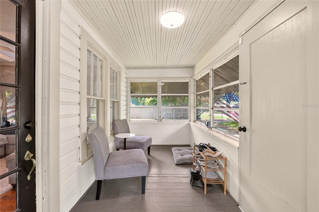 A sunroom features a gray wood floor, two armchairs, a shoe rack, and large windows — 18727 NW 251ST STREET, HIGH SPRINGS, FL