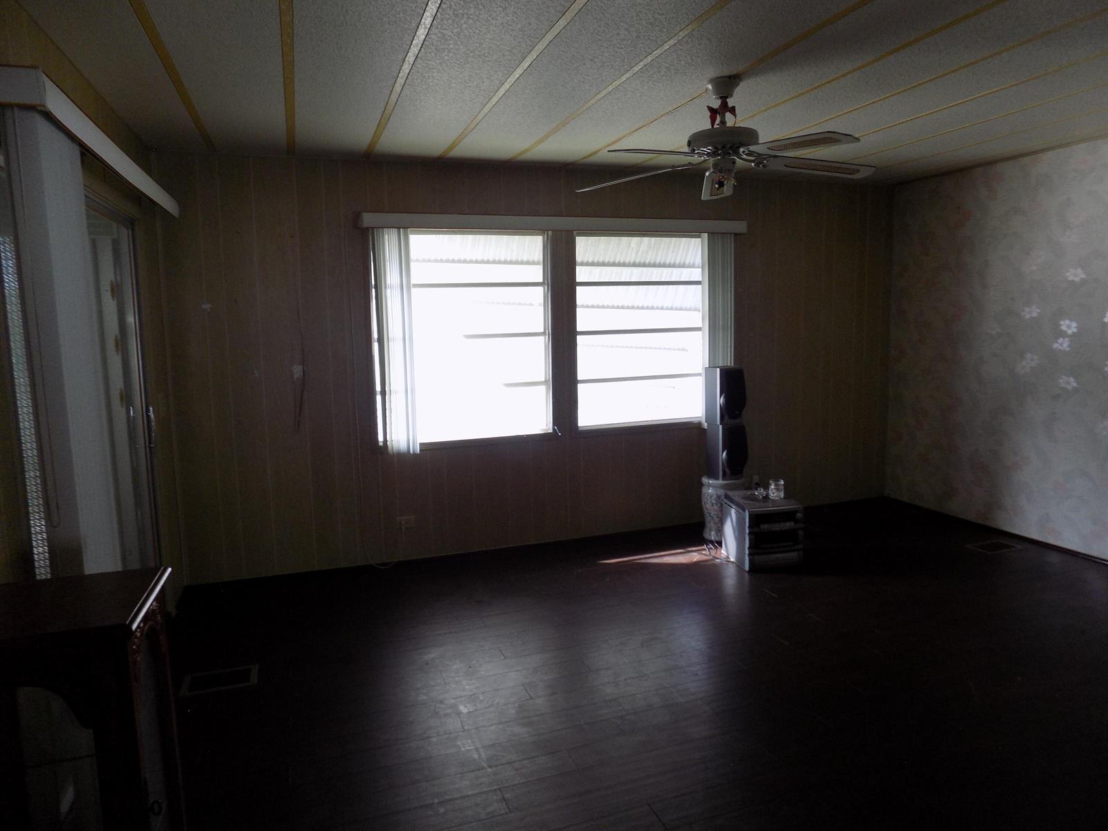 An empty living room features dark wood flooring, paneled walls, and a ceiling fan — 18009 Huapi, Boynton Beach FL 33436, BOYNTON BEACH, FL
