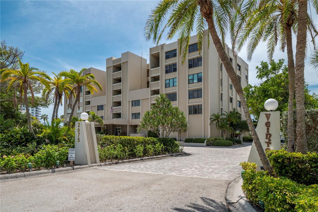 A multi-story beige apartment building stands behind a paved entrance with palm trees — 2675 GULF OF MEXICO DRIVE UNIT 204, LONGBOAT KEY, FL