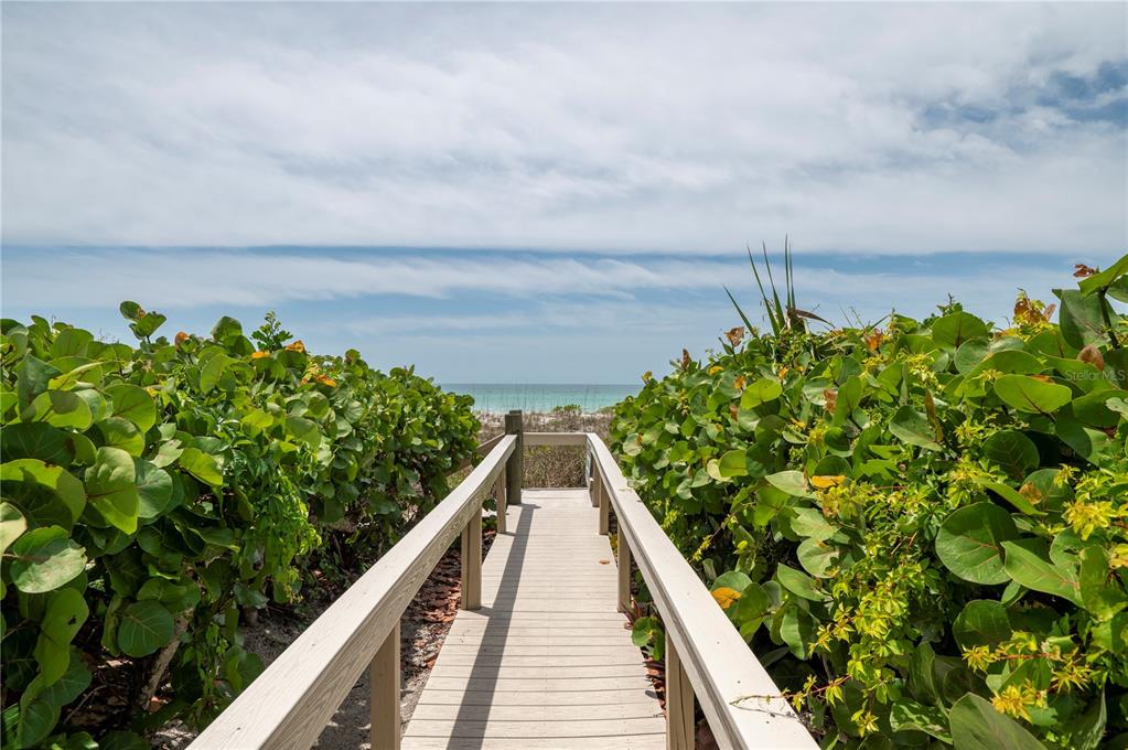 A wooden boardwalk leads through lush green foliage toward a view of the ocean — 2675 GULF OF MEXICO DRIVE UNIT 204, LONGBOAT KEY, FL
