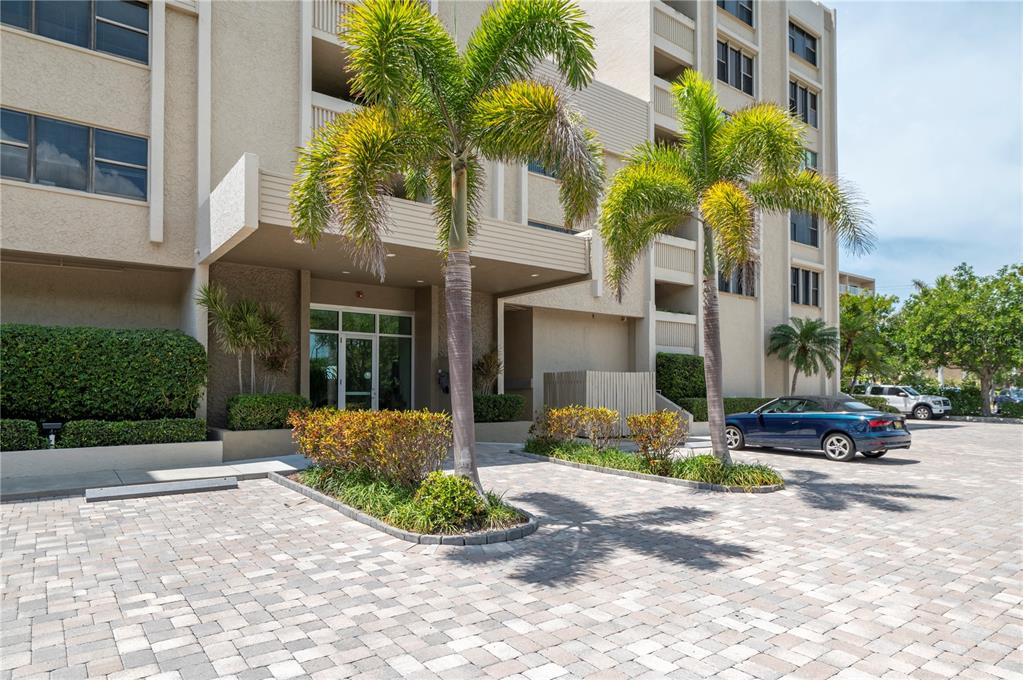 A paved driveway leads to the entrance of a multi-story apartment building with palm trees — 2675 GULF OF MEXICO DRIVE UNIT 204, LONGBOAT KEY, FL