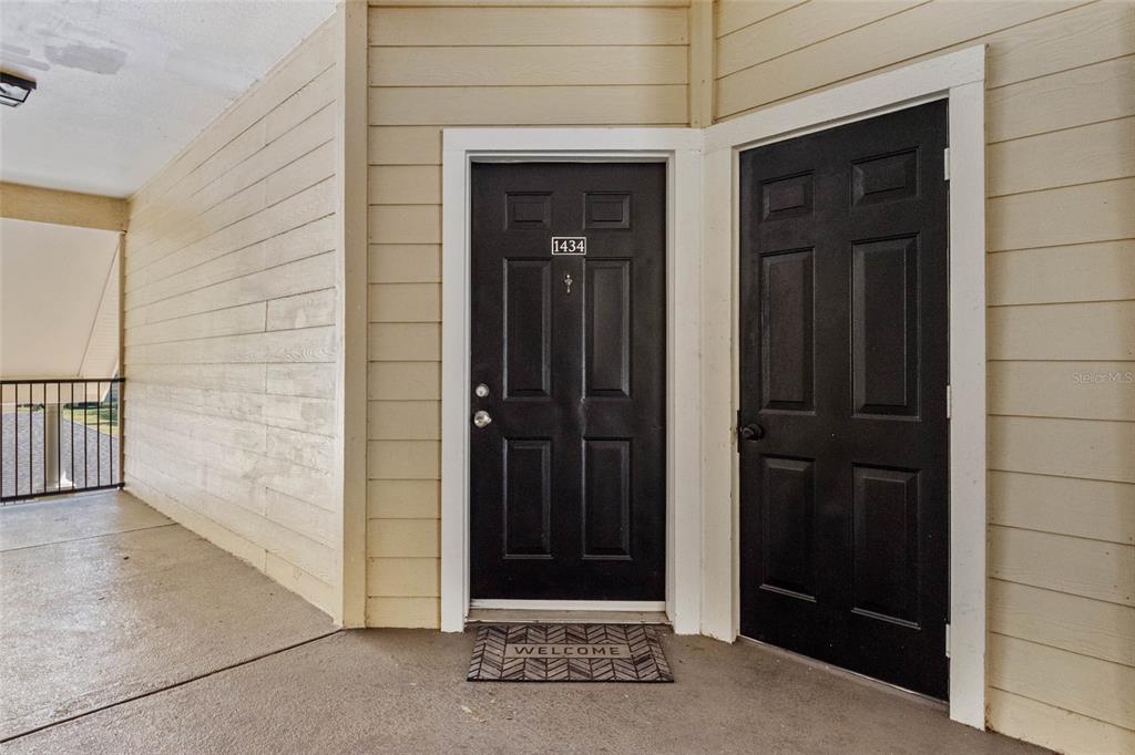 Two black doors with white trim are set against beige horizontal siding on a balcony — 2558 ROBERT TRENT JONES DRIVE UNIT 1434, ORLANDO, FL
