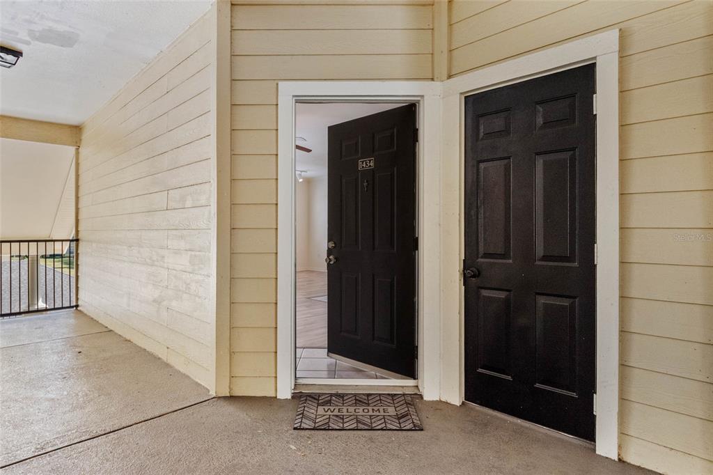 An open door reveals an apartment interior next to a closed door on a balcony — 2558 ROBERT TRENT JONES DRIVE UNIT 1434, ORLANDO, FL