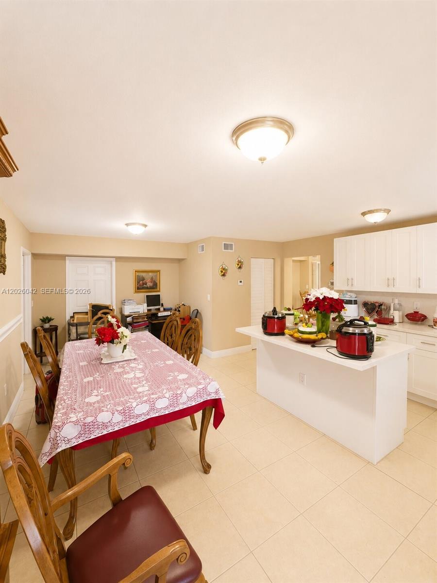 This kitchen and dining area features white cabinets, a central island, and tile flooring — 5551 E 4th Ave, Hialeah FL 33013, HIALEAH, FL