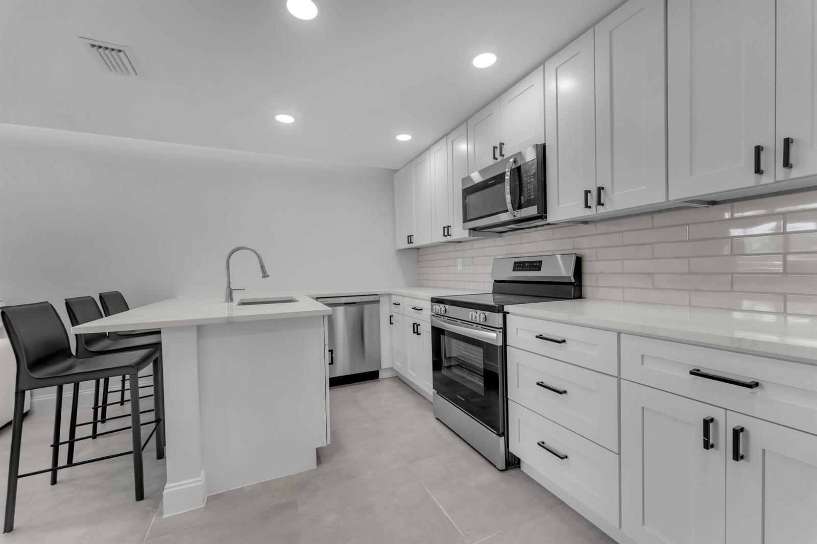 A modern kitchen features white shaker cabinets, stainless steel appliances, and a quartz-topped island — 381 SE 15th Avenue # 1, Deerfield Beach FL 33441, DEERFIELD BEACH, FL