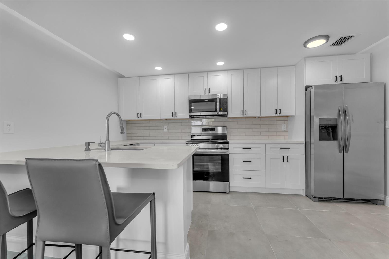 A modern kitchen features white cabinetry, stainless steel appliances, a quartz island, and gray flooring — 381 SE 15th Avenue # 1, Deerfield Beach FL 33441, DEERFIELD BEACH, FL