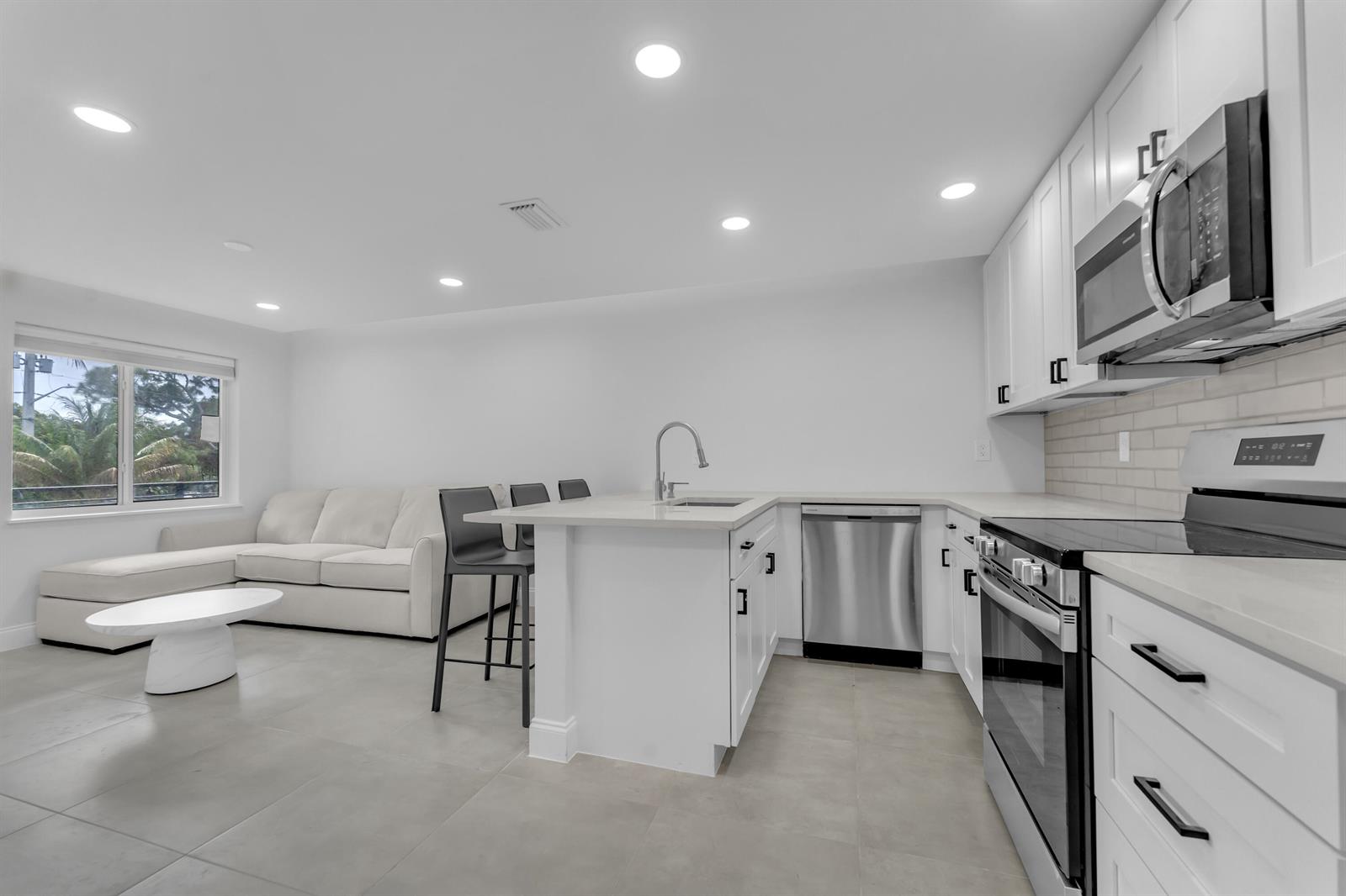 A modern kitchen with white cabinets, stainless steel appliances, and an island with bar seating — 381 SE 15th Avenue # 1, Deerfield Beach FL 33441, DEERFIELD BEACH, FL